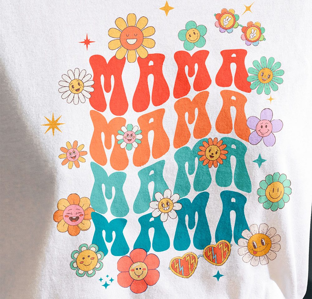 A woman wearing a white t-shirt customized with a DTF transfer of cartoon flowers and the word "Mama" in bright, vibrant colors.