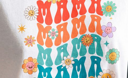 A woman wearing a white t-shirt customized with a DTF transfer of cartoon flowers and the word "Mama" in bright, vibrant colors.