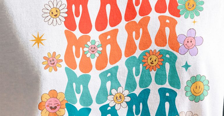 A woman wearing a white t-shirt customized with a DTF transfer of cartoon flowers and the word "Mama" in bright, vibrant colors.